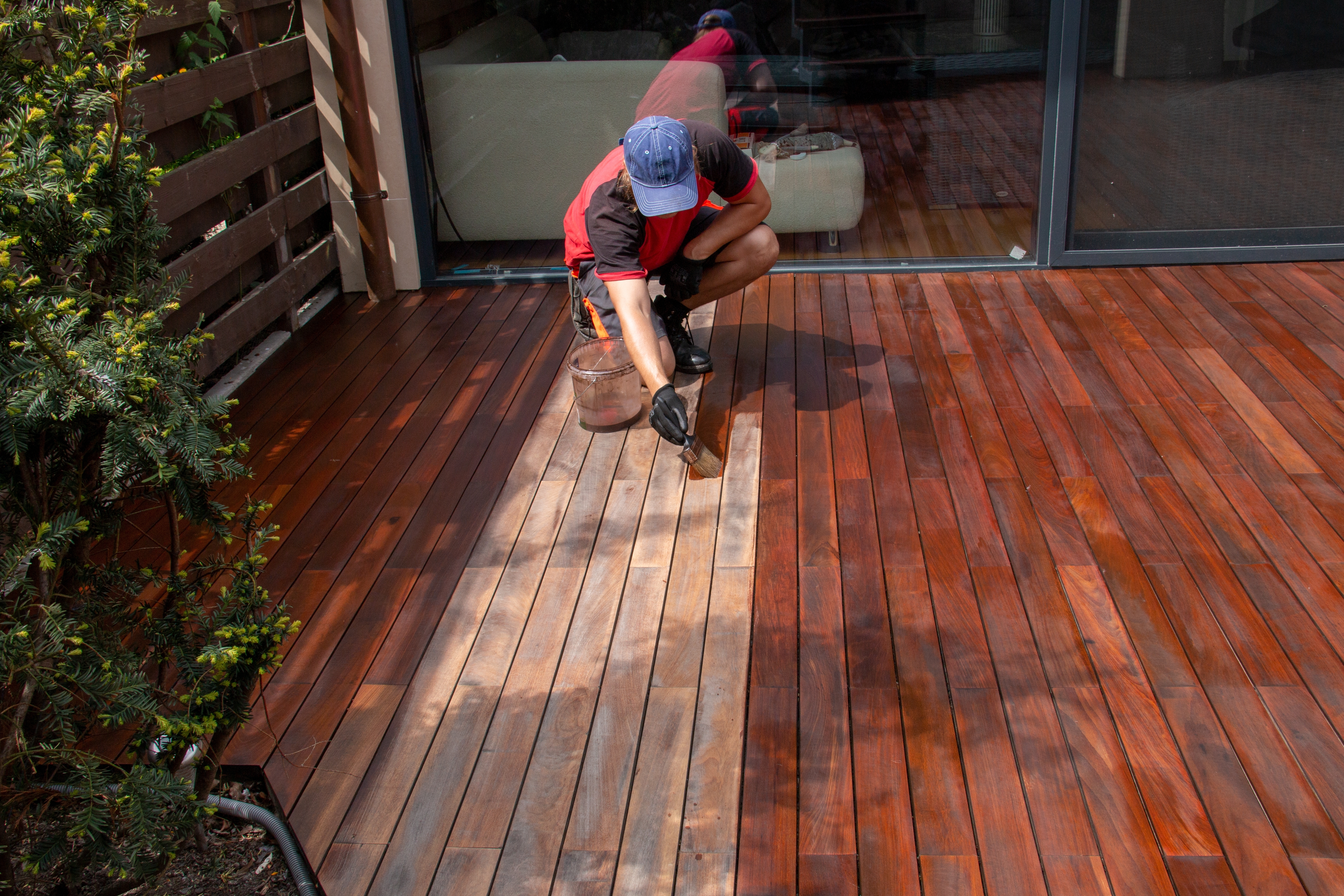 Worker staining wooden deck surface during outdoor decking installation Tauranga